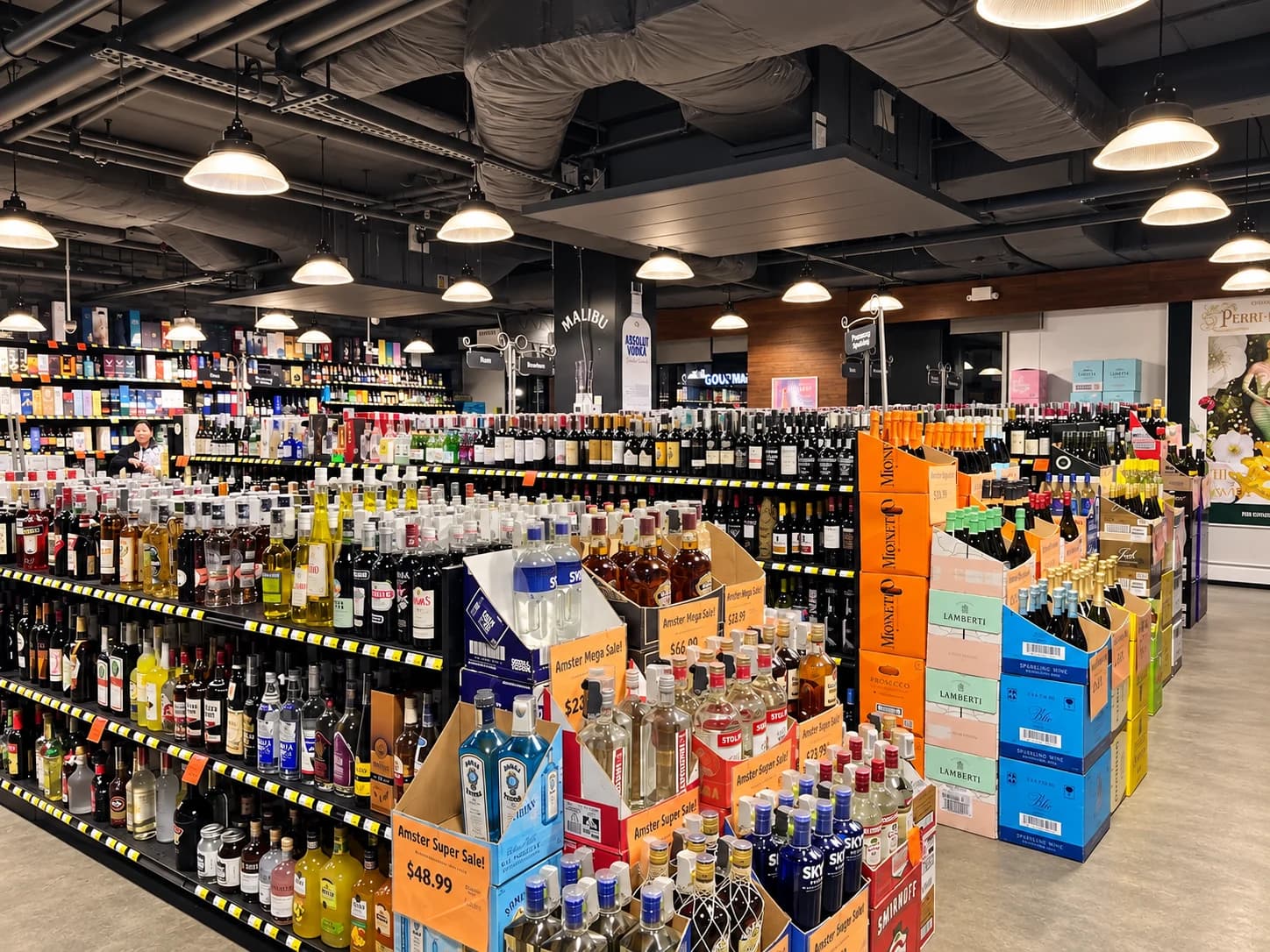Rows of wine and spirits at Amster Wine, with sparkling wine displays and orange sale signs.
